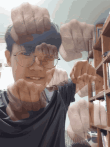 a man wearing glasses holds his fist up in front of a book shelf
