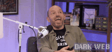 a man is sitting in front of a microphone wearing a shirt that says deus the grin .