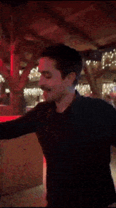 a man in a black shirt is dancing in a room with christmas lights on the ceiling .