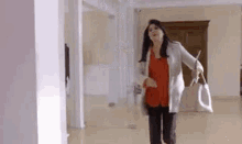 a woman is walking down a hallway holding a mop and a purse .