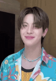 a young man wearing a floral shirt and a blue necklace is smiling .