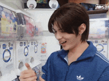 a young man wearing a blue adidas jacket is giving a thumbs up