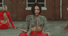 a woman in a zebra print top and red skirt is sitting on the ground