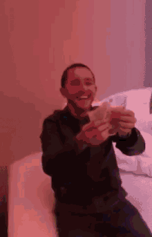 a man is sitting on a bed holding two glasses of beer in his hand .