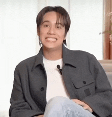 a young man is sitting on a couch and smiling while wearing a jacket .