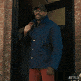 a man wearing sunglasses and a hat stands in front of a door that says netflix on it