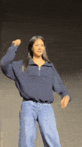 a woman wearing a blue sweater and jeans is dancing on a stage