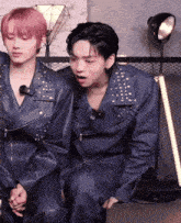 two young men are sitting next to each other wearing leather jackets and holding hands