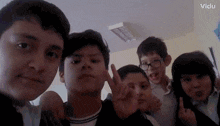 a group of young boys are posing for a picture in a classroom while giving the peace sign .