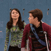 a boy with crutches is standing next to a girl in front of blue lockers that say ' lockers ' on them