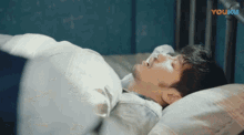 a man is laying in a bed with a youku logo behind him