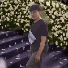 a young man wearing glasses and a black shirt is walking down stairs in front of a bush of flowers .