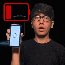 a man with glasses holds up a cell phone with a battery icon on the screen