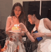 a woman blows out candles on a cake while another woman looks on