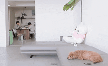 a teddy bear sits on a couch in a living room with two men sitting at a table