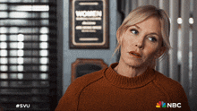 a woman in a brown sweater stands in front of a sign that says women on it