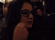 a woman with glasses is covering her mouth with her hand in a dark room