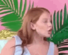 a woman with red hair is standing in front of a pink background with palm trees .
