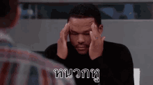 a man is holding his head in pain while sitting at a table .