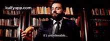 a man in a suit and tie is holding a sandwich and saying it 's unbelievable in front of a library .
