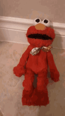 a red elmo stuffed animal is laying on a tiled floor