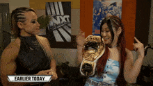two women standing in front of a nxt poster