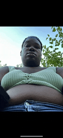 a man wearing a green top and blue shorts looks down at his belly