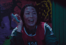 a woman with blood on her face is wearing a red vest with the number 124 on it