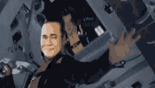 a man in a suit is smiling and waving while sitting in a plane