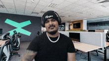 a man wearing headphones and a beanie has a x on the wall in the background