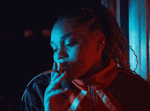 a woman in a red and black jacket is smoking a cigarette in a dark room .