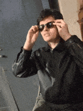 a man wearing sunglasses and a leather jacket has the letter o on his shirt