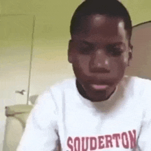 a young man wearing a white shirt with the word souderton on it is looking at the camera .