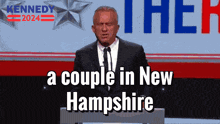 a man in a suit and tie stands at a podium with the words " a couple in new hampshire " below him