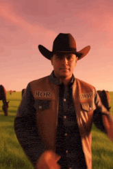 a man wearing a cowboy hat and a leather vest with aor on it