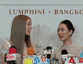 two women standing in front of microphones in front of a sign that says lumphini bangkok