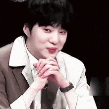 a young man in a suit and tie is sitting with his hands folded and making a funny face .