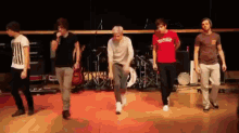 a group of young men are dancing on a stage and one of them is wearing a red shirt that says one direction on it