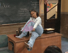 a woman sits on a desk in front of a chalkboard with the word week written on it