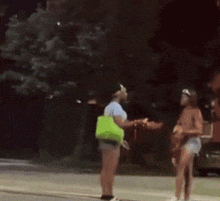 a woman in a green bag is standing on the sidewalk next to a man .