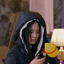a woman wearing a hooded jacket is holding a yellow duck