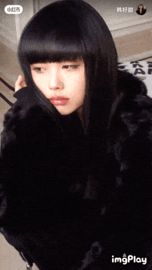 a woman with long black hair and bangs is wearing a black fur coat and looking at the camera