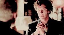 a man with his hands folded looks at another man in a room