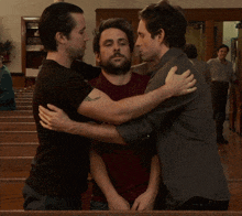 three men are hugging each other in a church with one wearing a shirt that says ' jesus ' on it