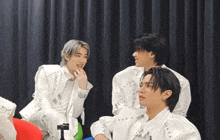 a group of young men are sitting in front of a black curtain and talking