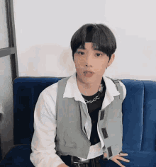 a young man is sitting on a blue couch wearing a white shirt and a grey vest