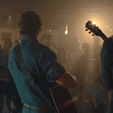 a man in a blue shirt is playing an acoustic guitar in front of a crowd