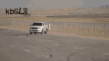 a white truck driving down a highway with kbsl written on the bottom