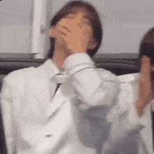 a man in a white suit and tie is covering his mouth .