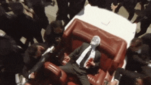a man in a suit and tie is laying on a red couch in a crowd of people